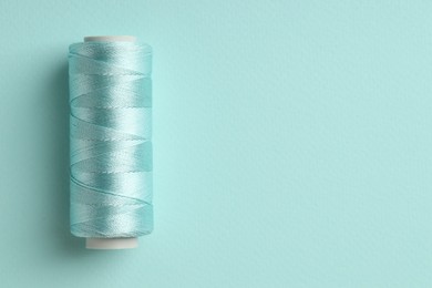 Photo of Spool of sewing thread on light blue background, top view. Space for text