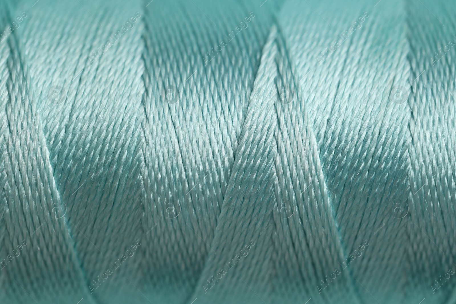 Photo of Spool of turquoise sewing thread as background, closeup