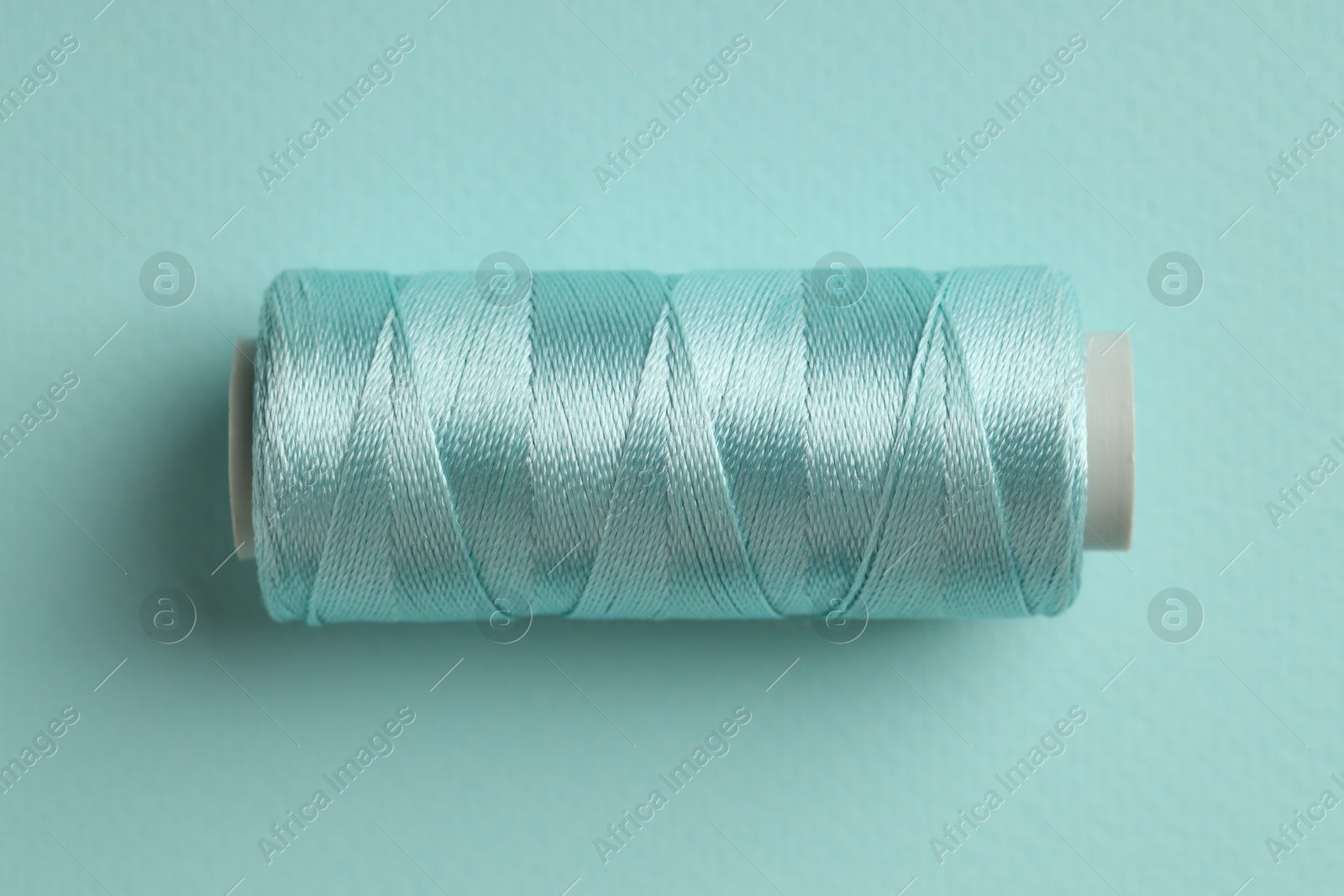 Photo of Spool of sewing thread on light blue background, top view