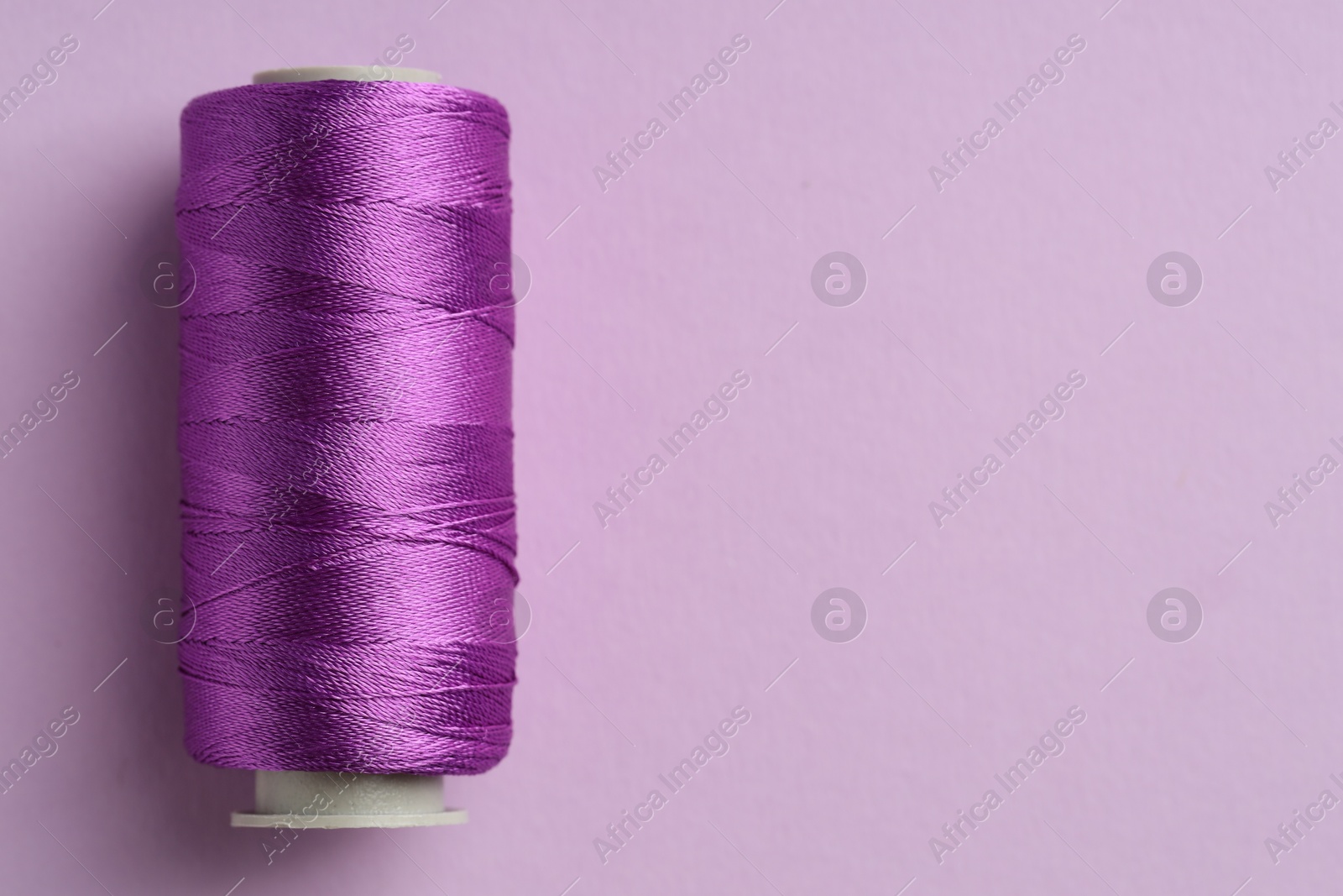 Photo of Spool of sewing thread on violet background, top view. Space for text