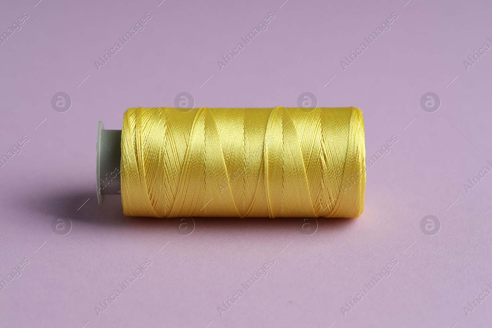 Photo of Spool of yellow sewing thread on violet background