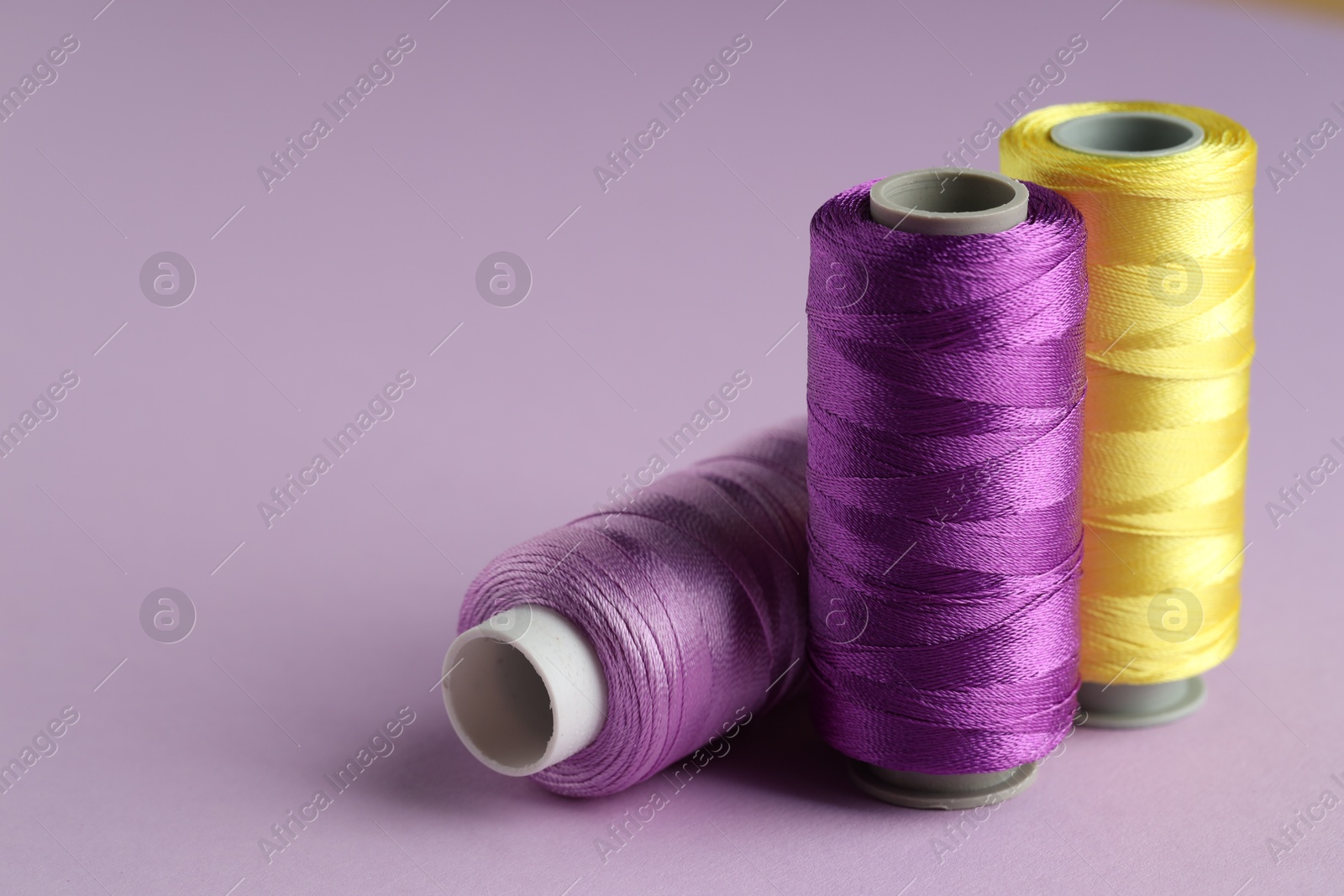 Photo of Different spools of sewing threads on violet background, closeup. Space for text