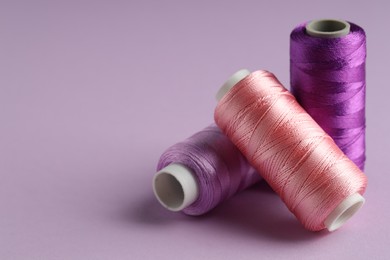 Photo of Different spools of sewing threads on violet background, closeup. Space for text