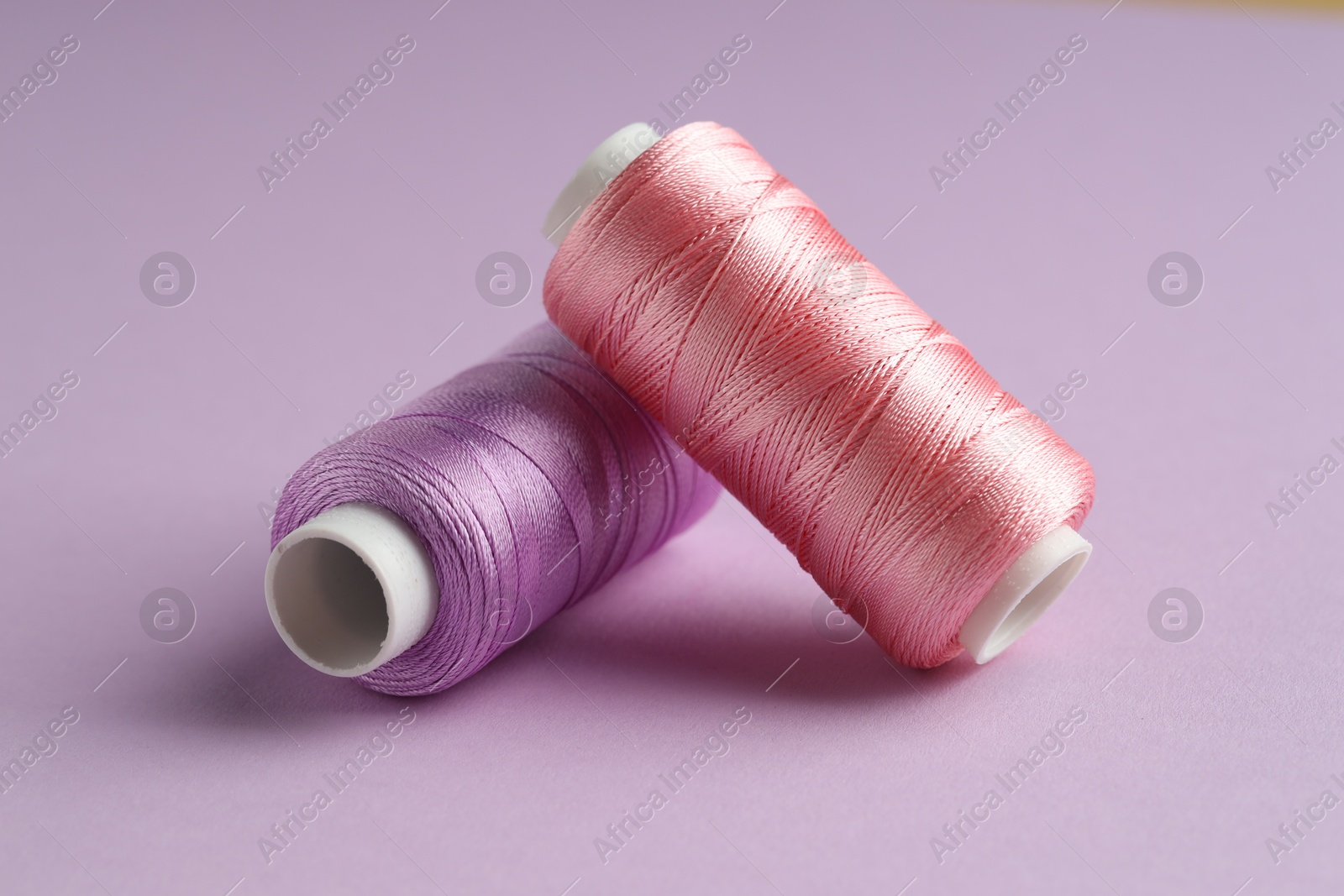 Photo of Different spools of sewing threads on violet background, closeup