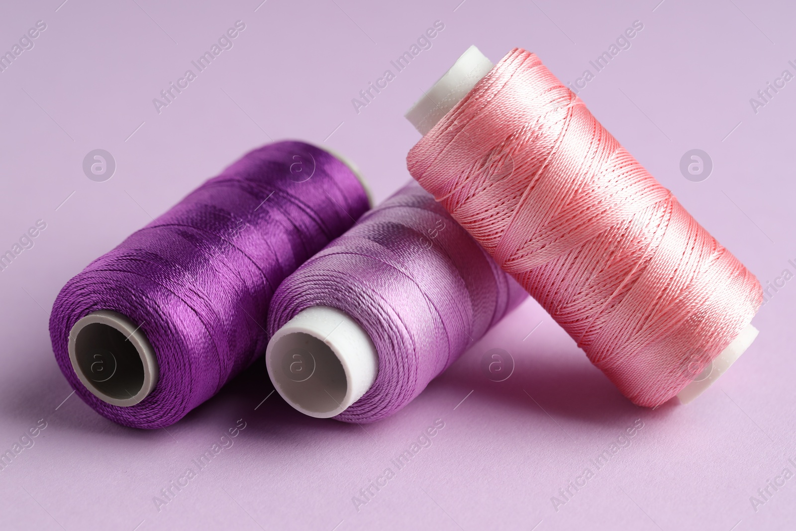 Photo of Different spools of sewing threads on violet background, closeup