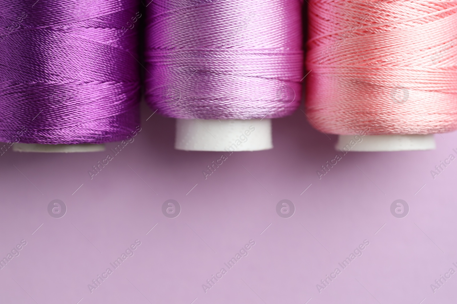 Photo of Different spools of sewing threads on violet background, flat lay. Space for text