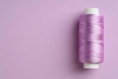 Photo of Spool of sewing thread on violet background, top view. Space for text