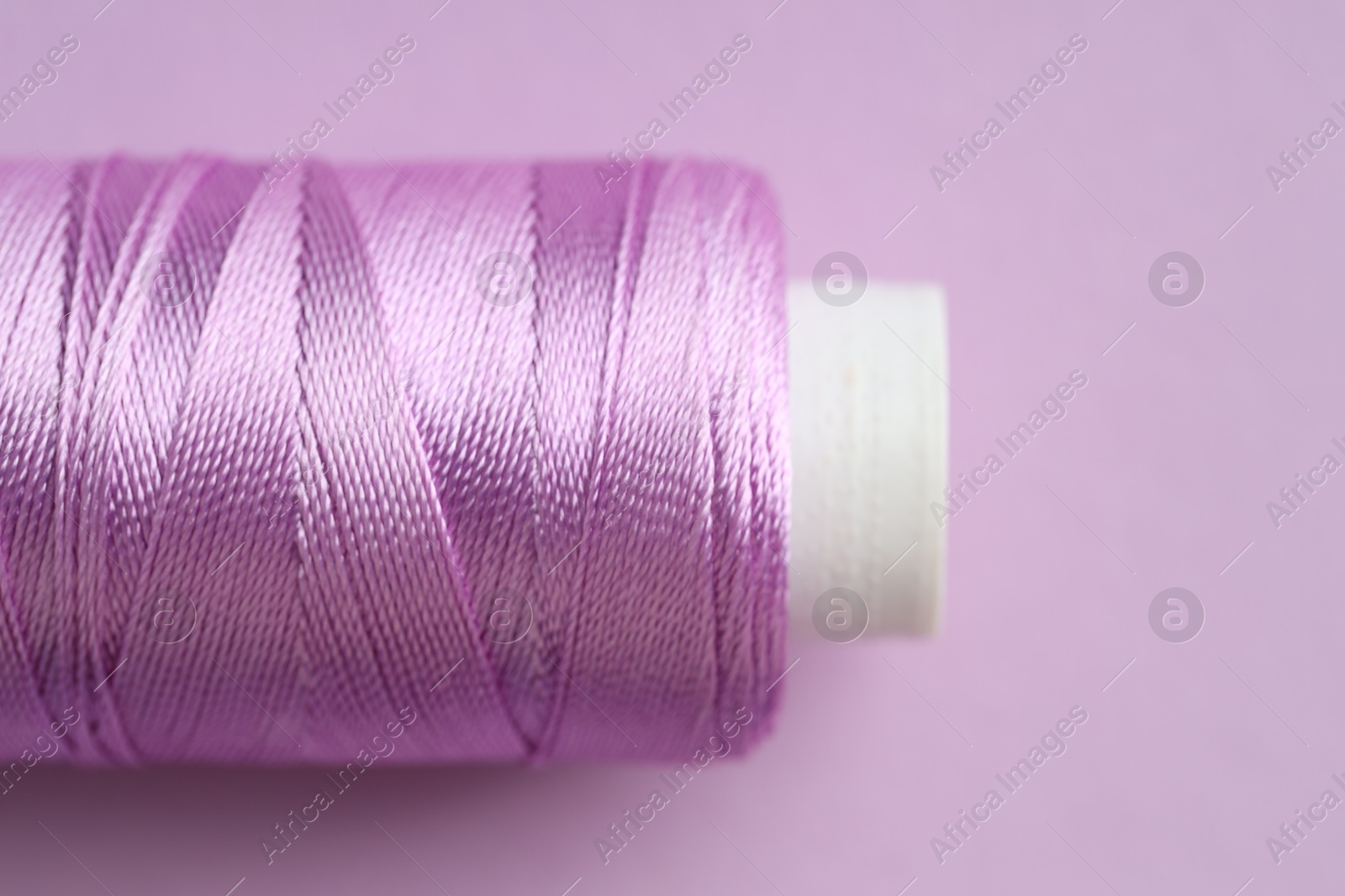 Photo of Spool of sewing thread on violet background, closeup. Space for text