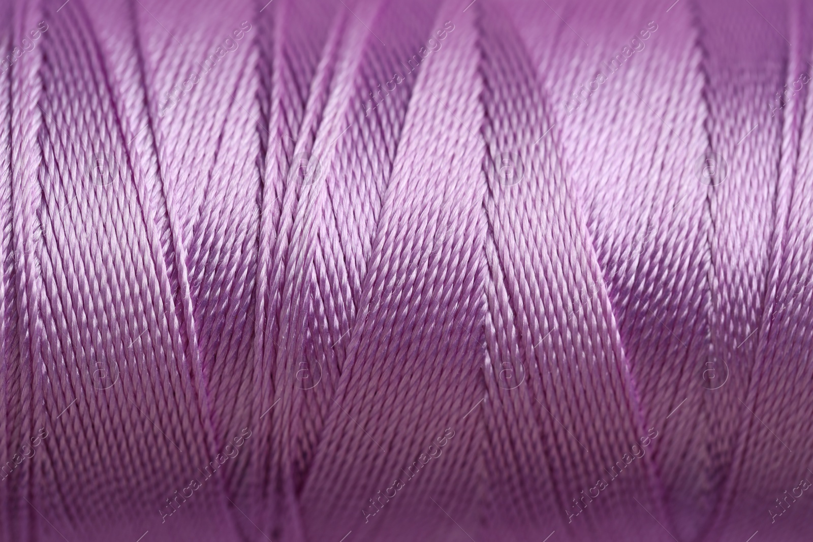 Photo of Spool of violet sewing thread as background, closeup