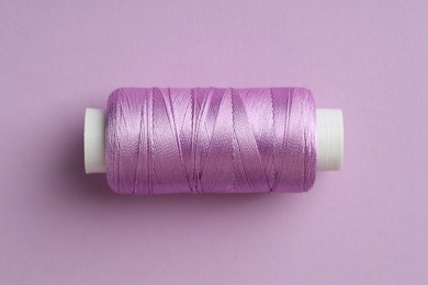 Photo of Spool of sewing thread on violet background, top view