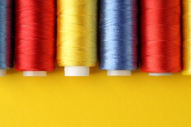 Photo of Different spools of sewing threads on yellow background, flat lay. Space for text