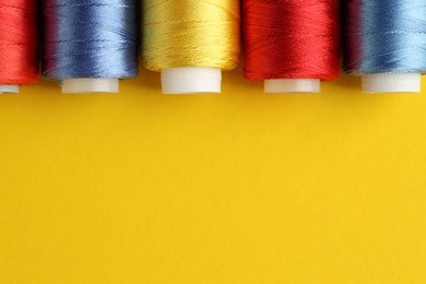 Photo of Different spools of sewing threads on yellow background, flat lay. Space for text