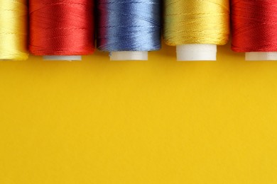 Photo of Different spools of sewing threads on yellow background, flat lay. Space for text