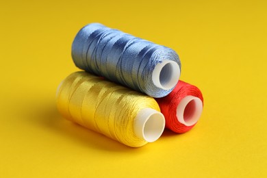 Photo of Different spools of sewing threads on yellow background, closeup