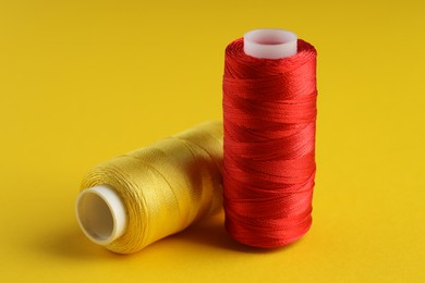 Photo of Different spools of sewing threads on yellow background, closeup