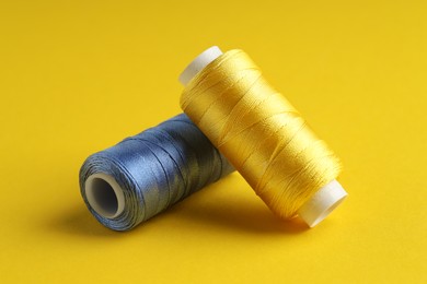 Photo of Different spools of sewing threads on yellow background, closeup