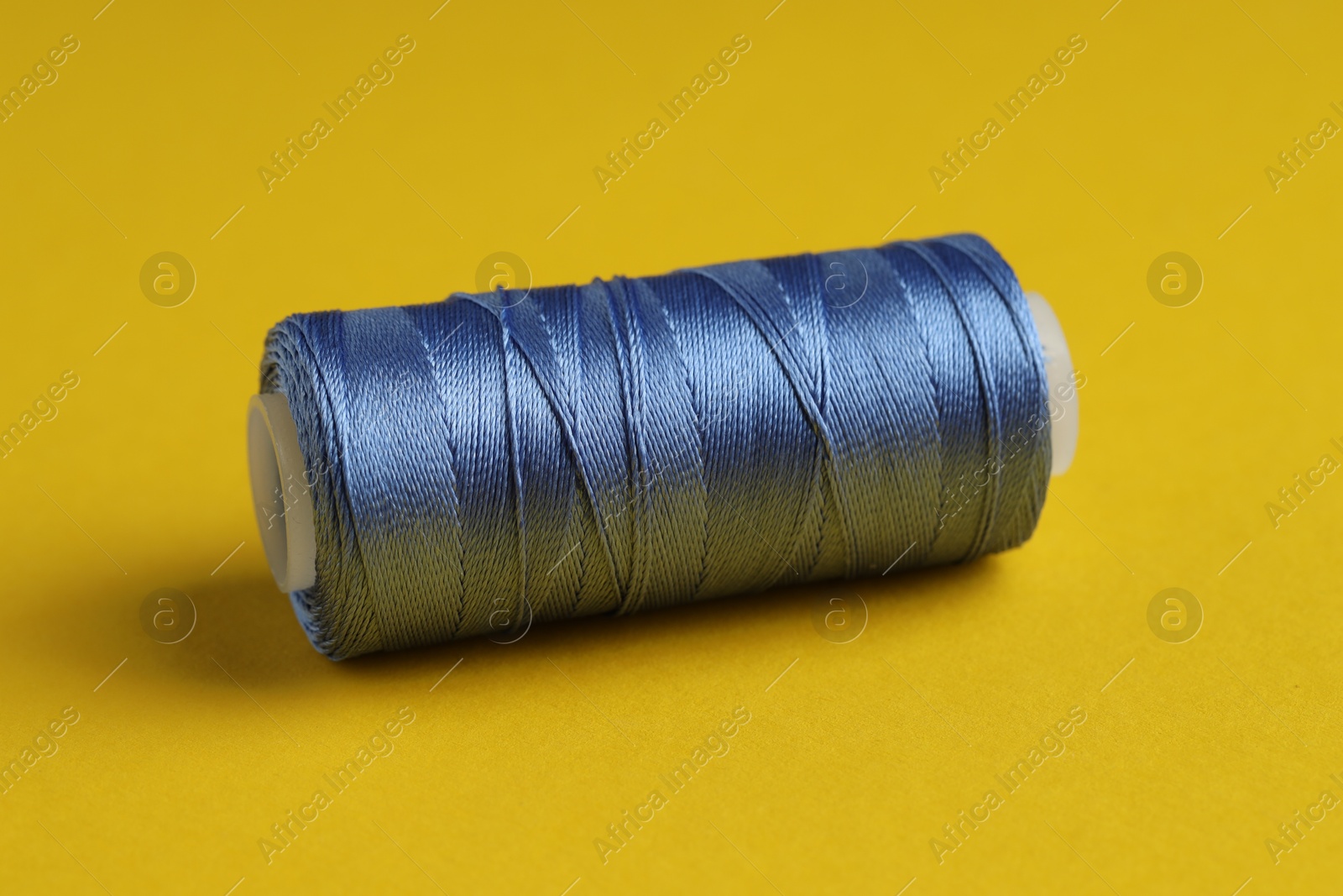 Photo of Spool of blue sewing thread on yellow background, closeup