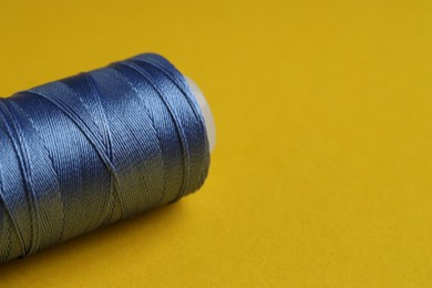 Photo of Spool of blue sewing thread on yellow background, closeup. Space for text