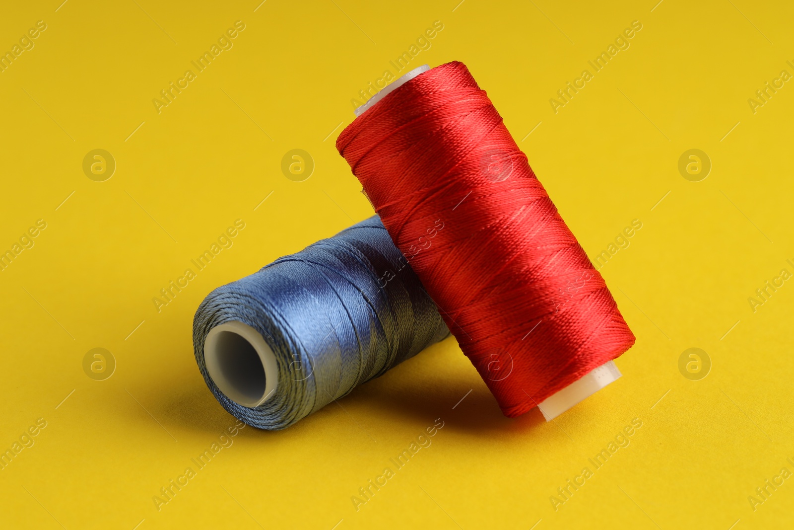 Photo of Different spools of sewing threads on yellow background, closeup