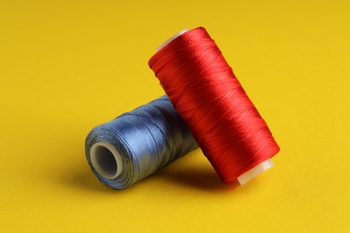 Photo of Different spools of sewing threads on yellow background, closeup