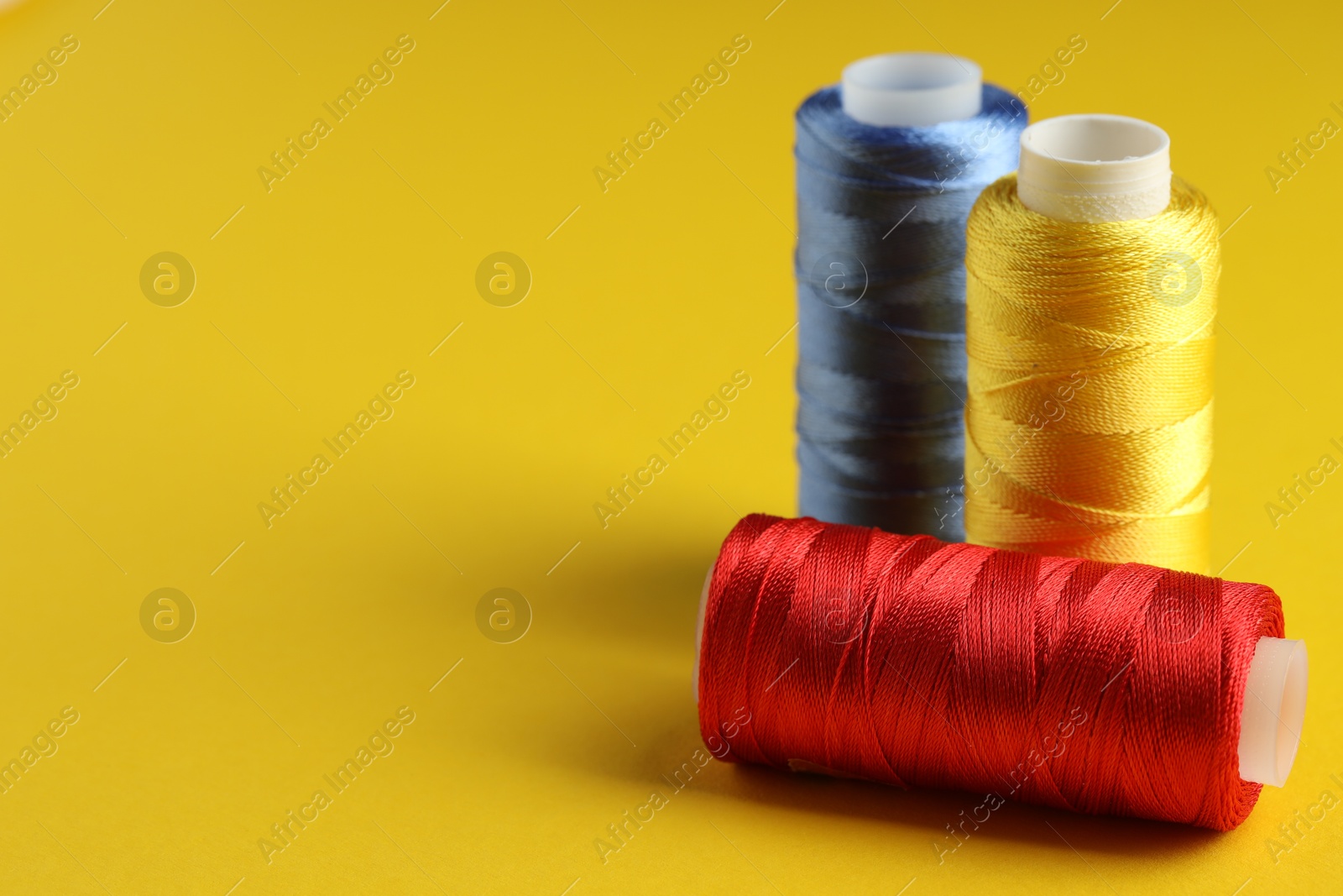 Photo of Different spools of sewing threads on yellow background, closeup. Space for text