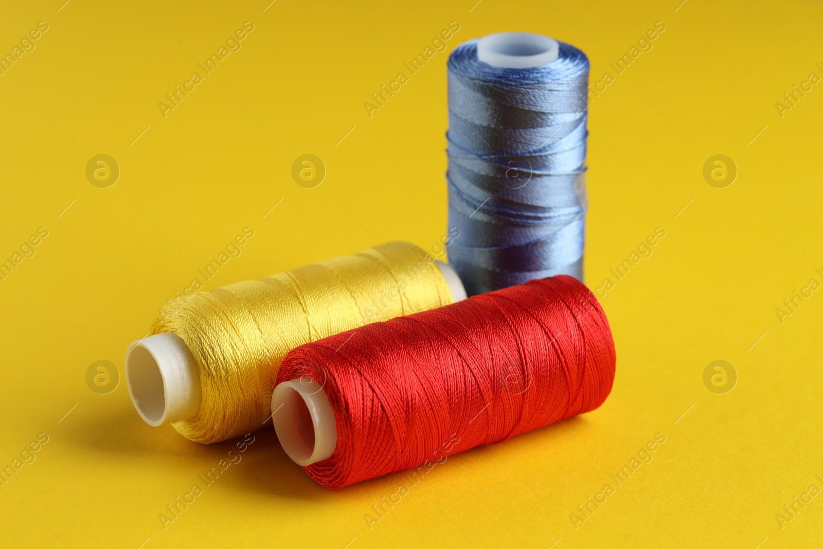 Photo of Different spools of sewing threads on yellow background, closeup