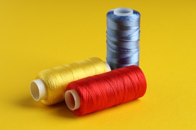 Photo of Different spools of sewing threads on yellow background, closeup