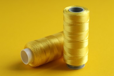 Photo of Spools of sewing threads on yellow background, closeup