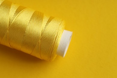 Photo of Spool of sewing thread on yellow background, closeup. Space for text