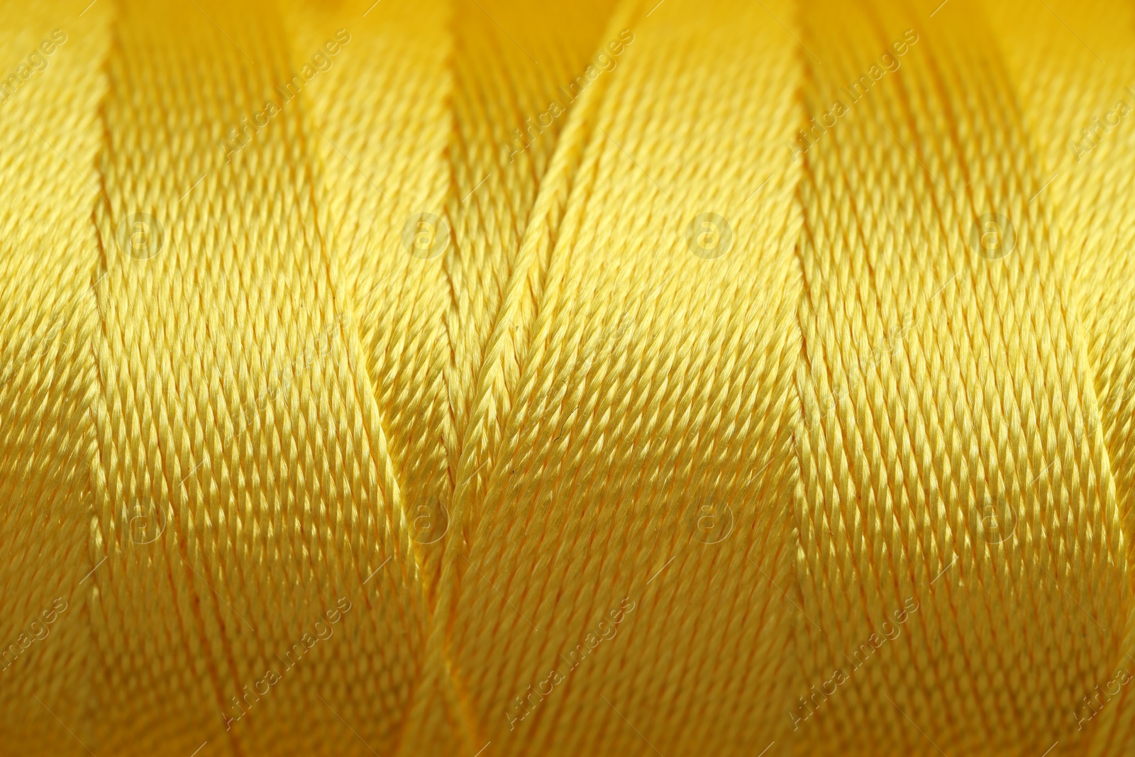 Photo of Spool of yellow sewing thread as background, closeup