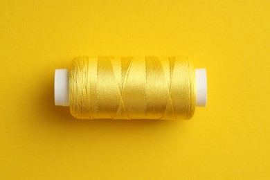 Photo of Spool of sewing thread on yellow background, top view