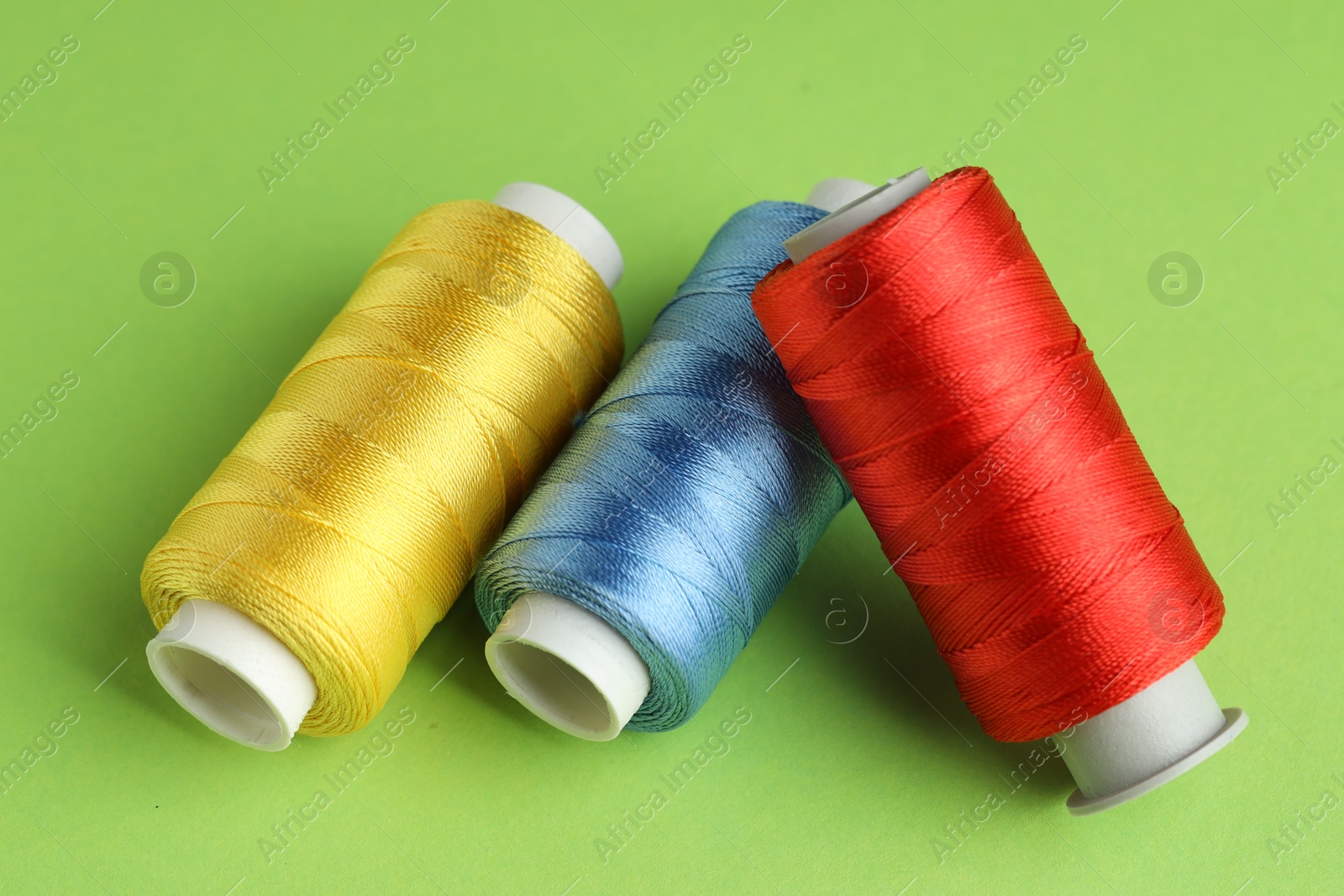 Photo of Different spools of sewing threads on green background, closeup