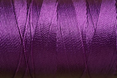 Photo of Spool of violet sewing thread as background, closeup