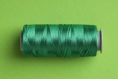 Photo of Spool of sewing thread on green background, top view