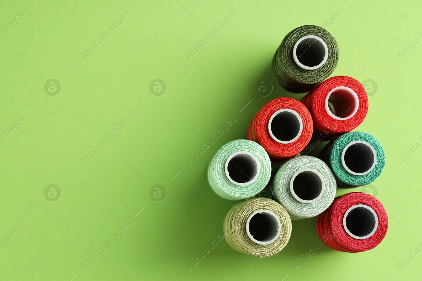 Photo of Different spools of sewing threads on green background, flat lay. Space for text