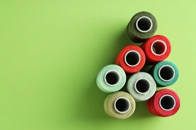 Photo of Different spools of sewing threads on green background, flat lay. Space for text