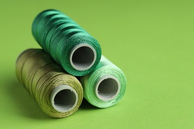 Photo of Spools of sewing threads on green background, closeup. Space for text