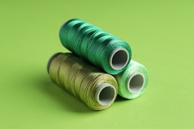 Photo of Spools of sewing threads on green background, closeup