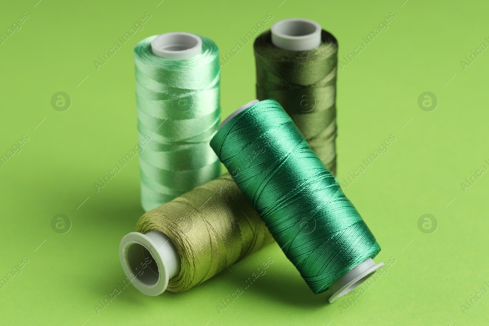 Photo of Spools of sewing threads on green background, closeup