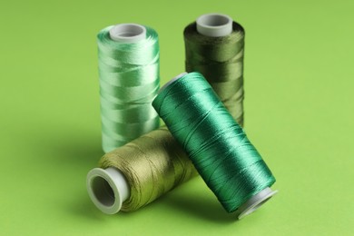 Photo of Spools of sewing threads on green background, closeup