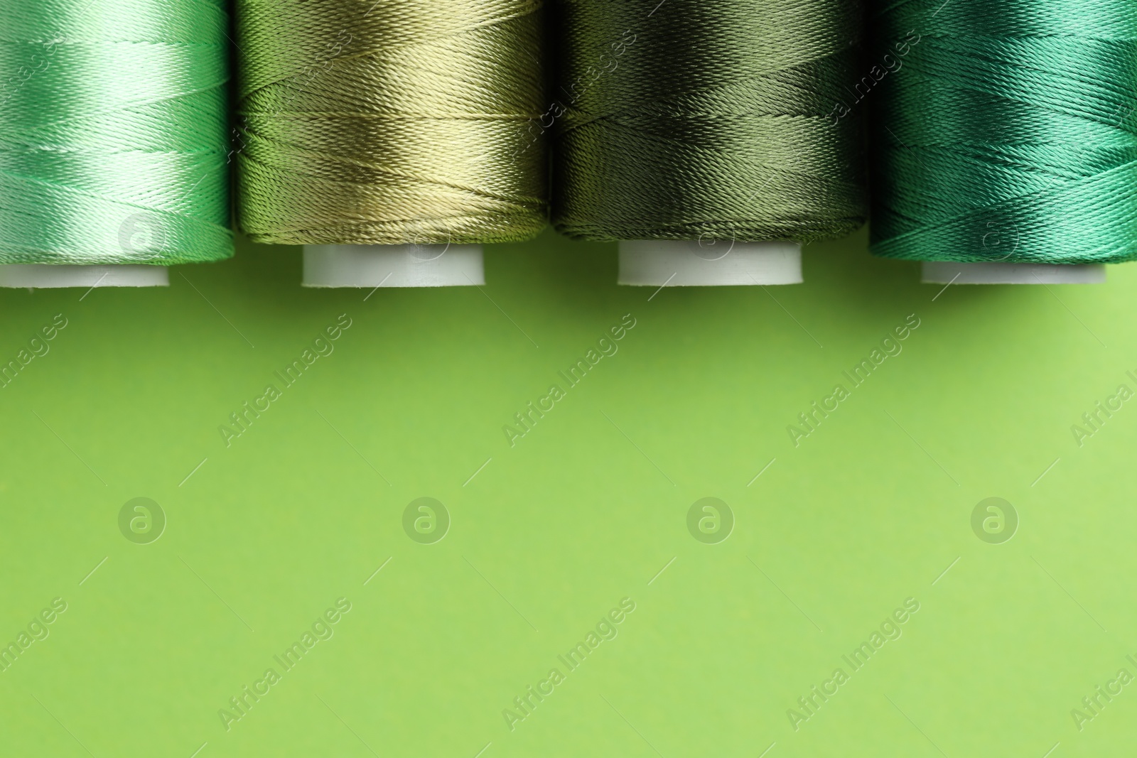 Photo of Spools of sewing threads on green background, flat lay. Space for text