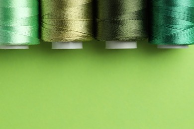 Photo of Spools of sewing threads on green background, flat lay. Space for text