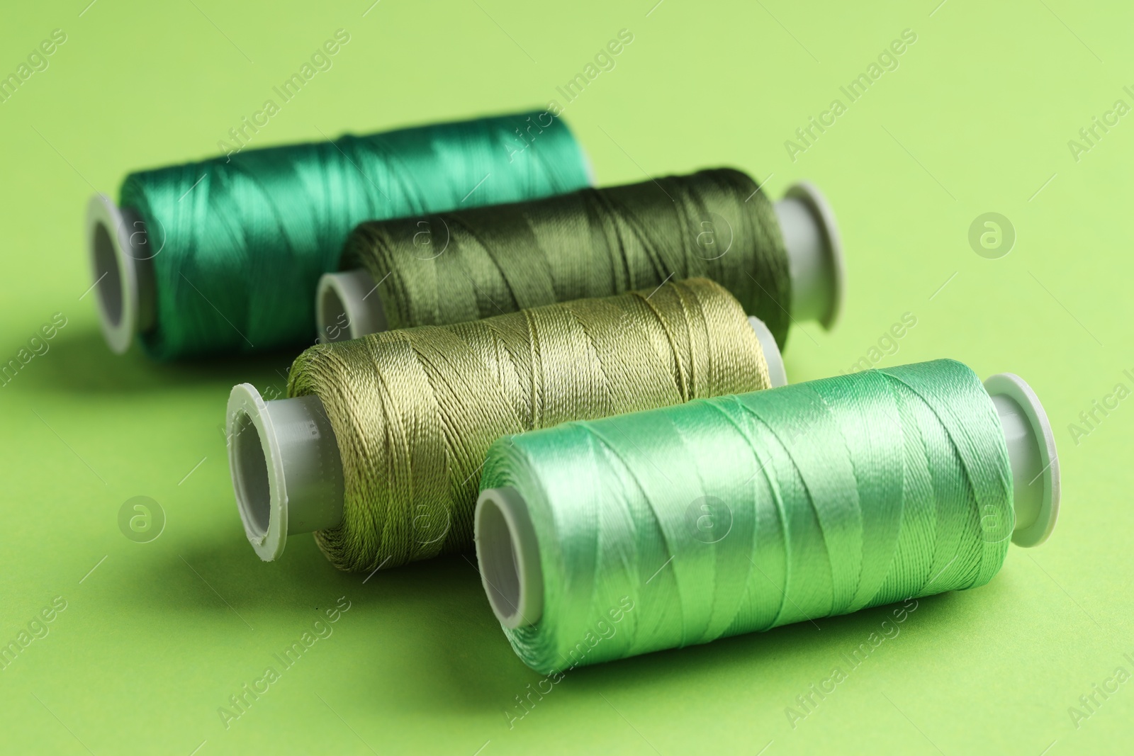 Photo of Spools of sewing threads on green background, closeup