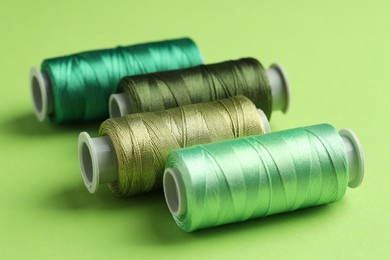 Photo of Spools of sewing threads on green background, closeup