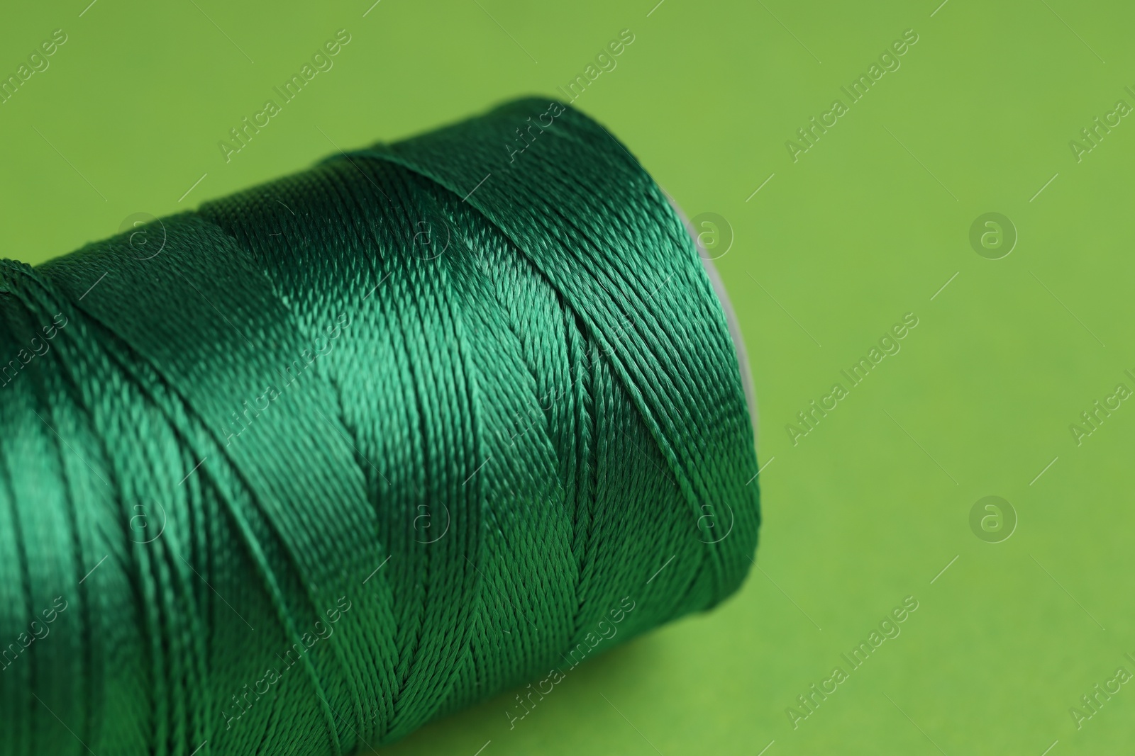 Photo of Spool of sewing thread on green background, closeup. Space for text