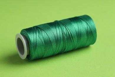 Photo of Spool of sewing thread on green background, closeup