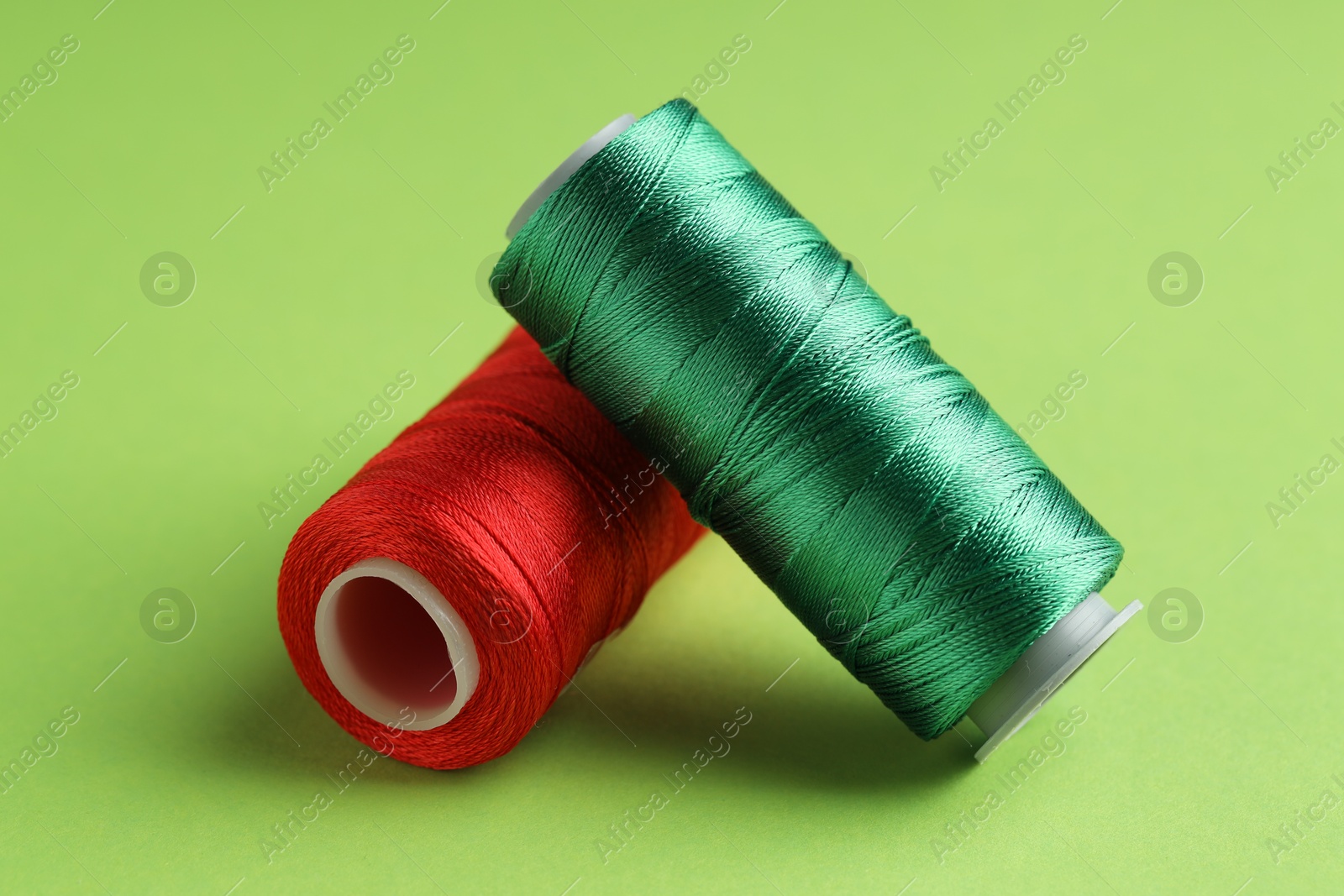 Photo of Different spools of sewing threads on green background, closeup