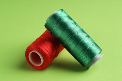 Photo of Different spools of sewing threads on green background, closeup