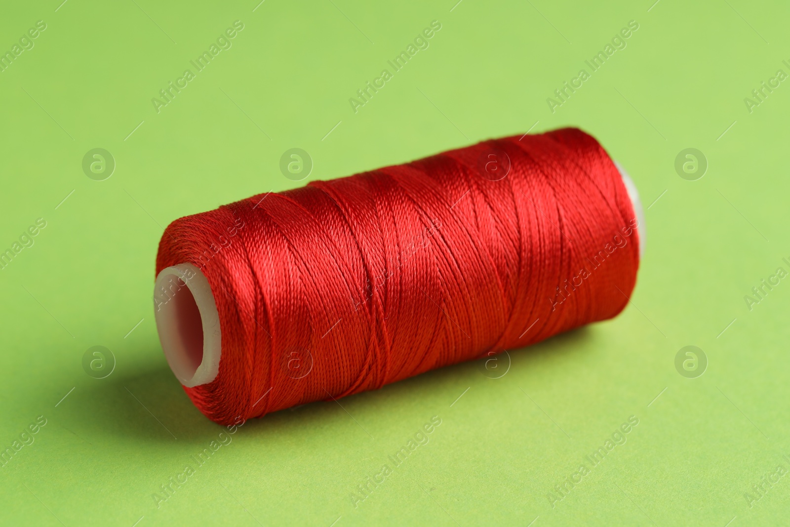 Photo of Spool of red sewing thread on green background, closeup