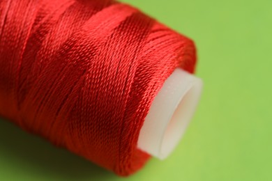 Photo of Spool of red sewing thread on green background, closeup